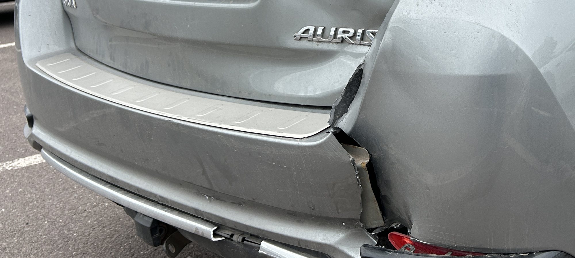 Aufgerissene hintere Stoßfängerecke eines silbernen Toyota Auris Kombi mit blankem Blech an der Bruchkante